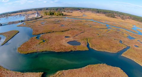 Aerial photo of brown marsh with blue water cutting through.  